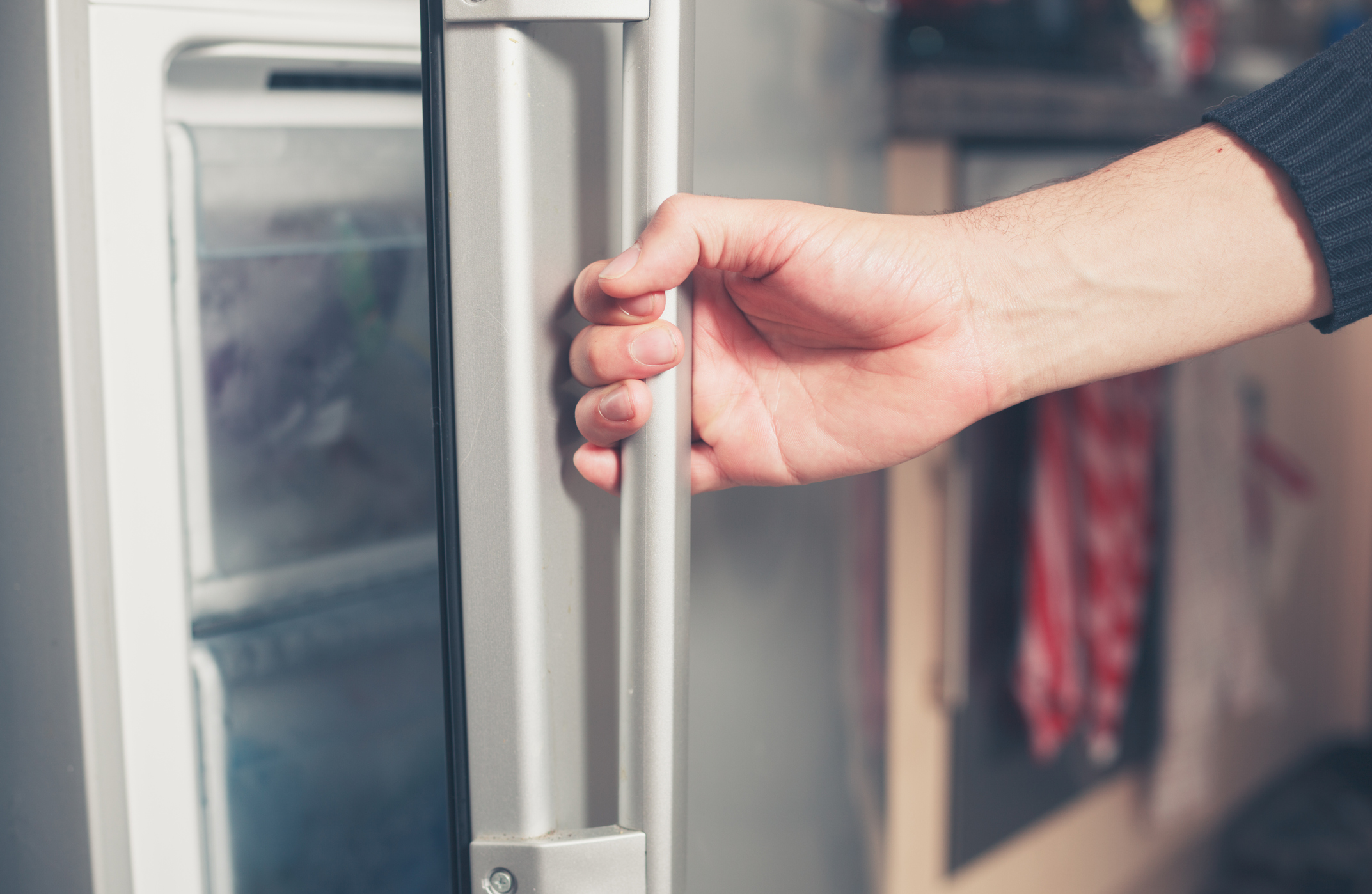 La mano de un varón joven abre la puerta de un congelador